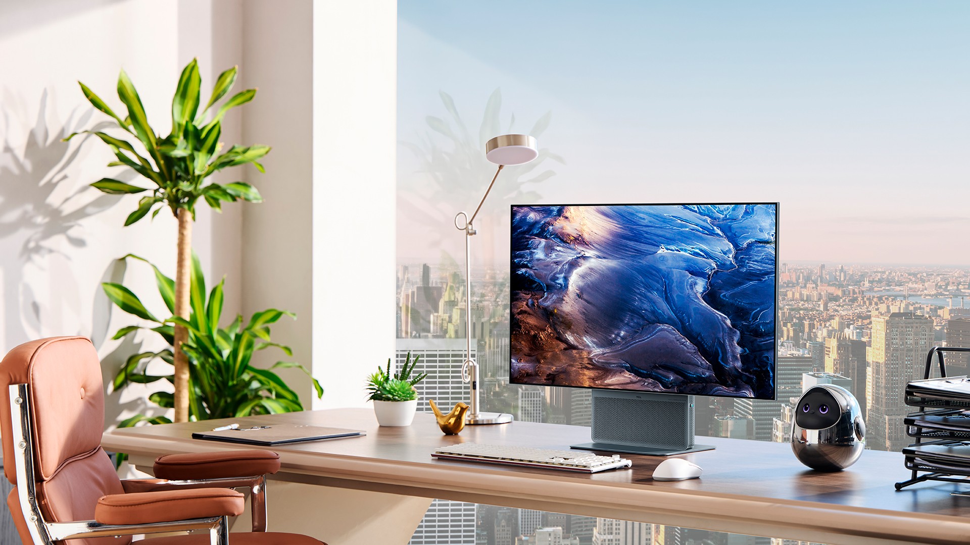 Modern office desk setup: curved wood desk, widescreen monitor displaying blue abstract imagery, keyboard, mouse, plant, and a small robotic device on the right with city skyline in the background.