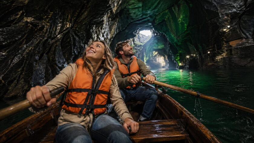 Туристы плывут на лодке по подземной части мраморного каньона Рускеала с изумрудной водой и подсвеченными скалами