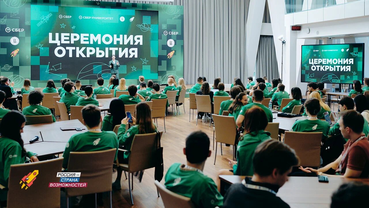 Большой зал с участниками в зелёных футболках на церемонии открытия; ведущий на сцене, большой экран с надписью 'ЦЕРЕМОНИЯ ОТКРЫТИЯ'.