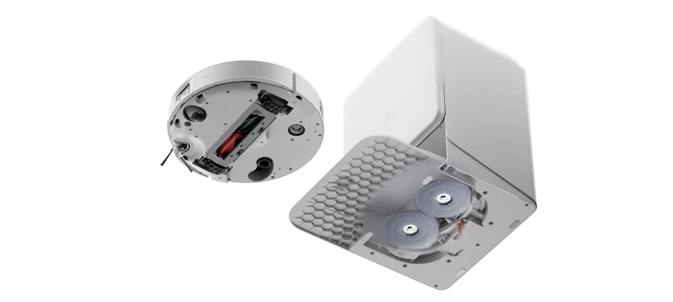 Exploded view of a compact white mechanical device showing a circular module separated from a rectangular housing with a honeycomb vent plate and two round grinding wheels/rollers nearby.