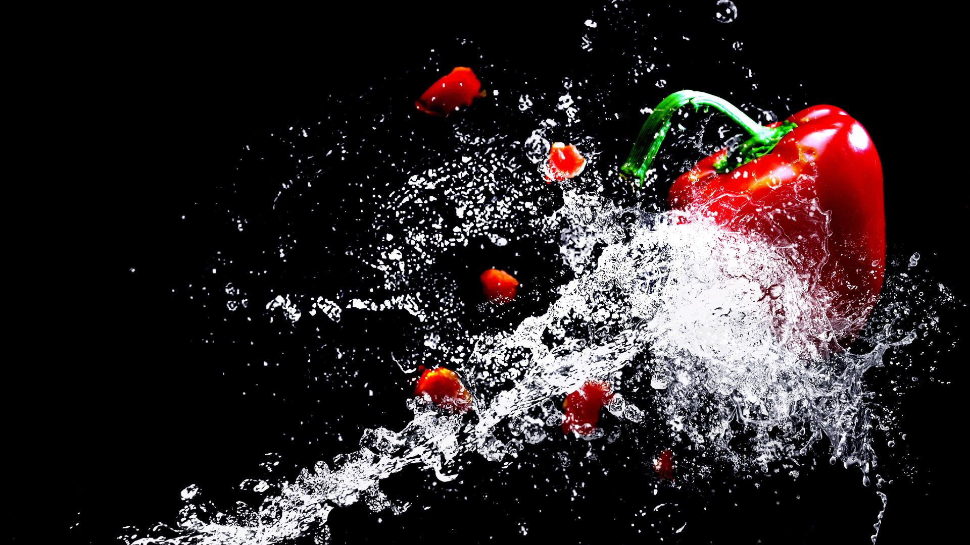 Red bell pepper and water droplets splashing against a black background.