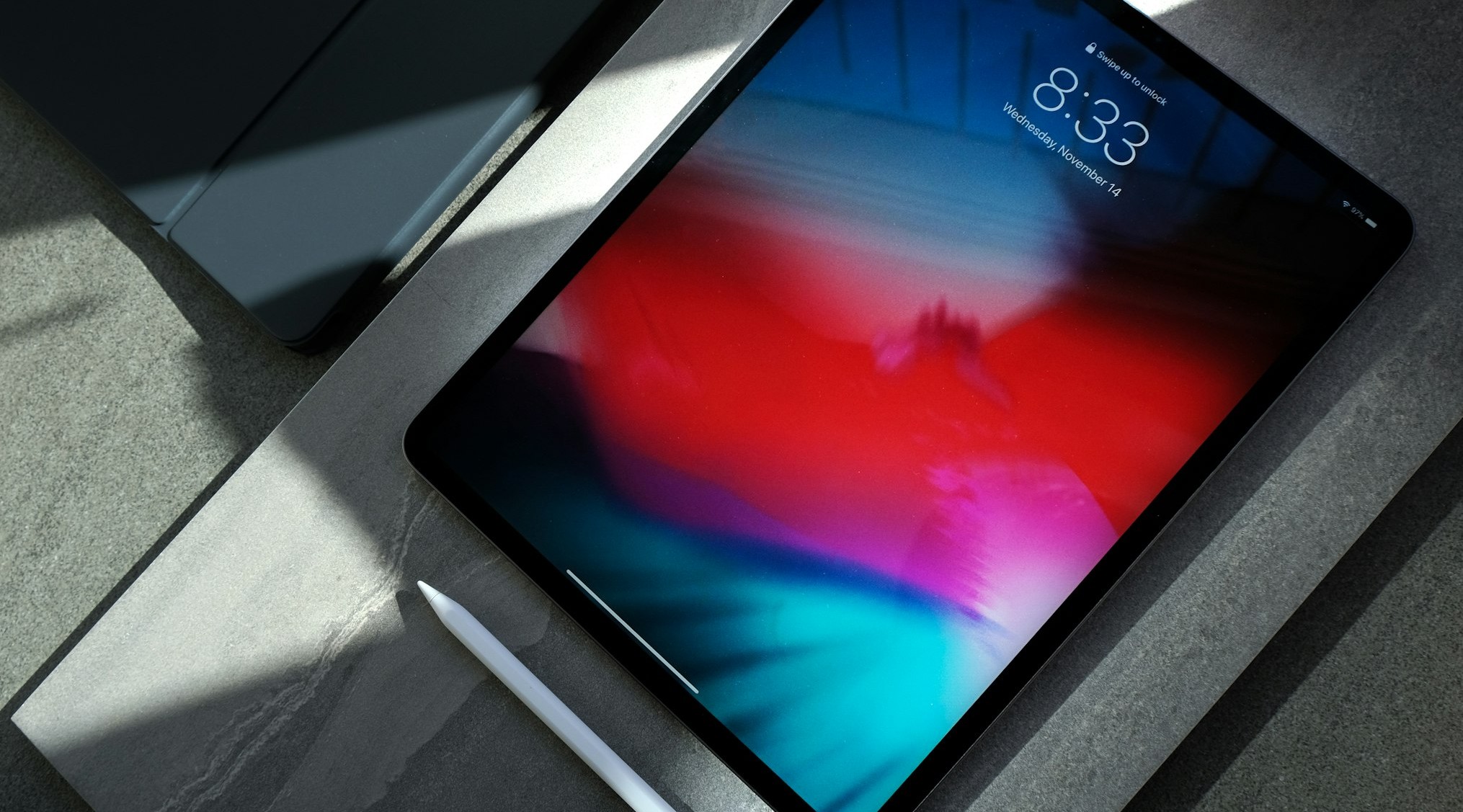 Close-up of a tablet with a vivid multicolor screen on a gray desk, with a white stylus nearby.