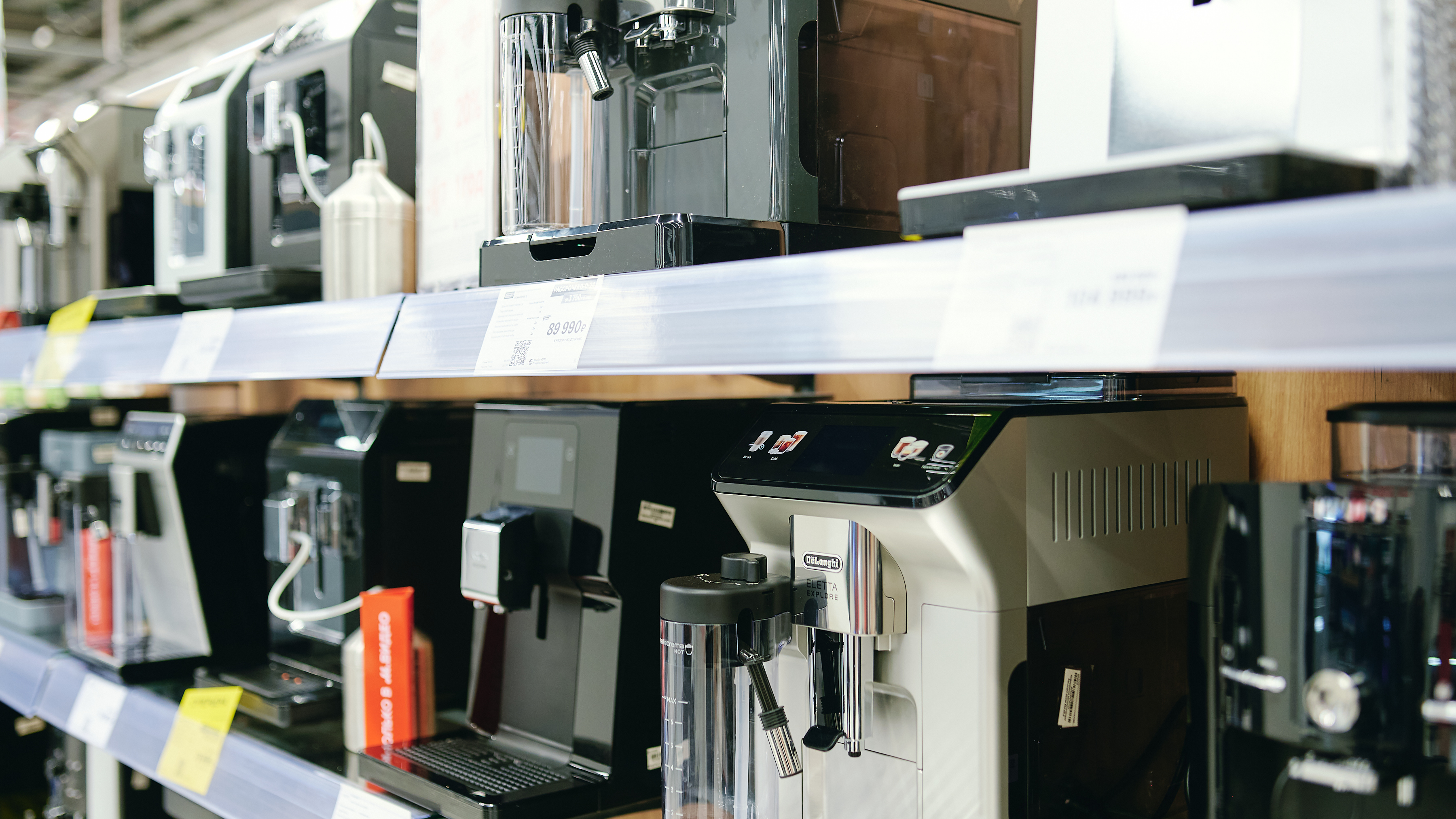 Row of coffee machines on display in a store, showcasing stainless steel and black models with price tags.
