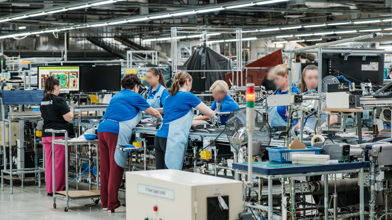 Factory assembly line with workers in blue uniforms assembling components on a conveyor.
