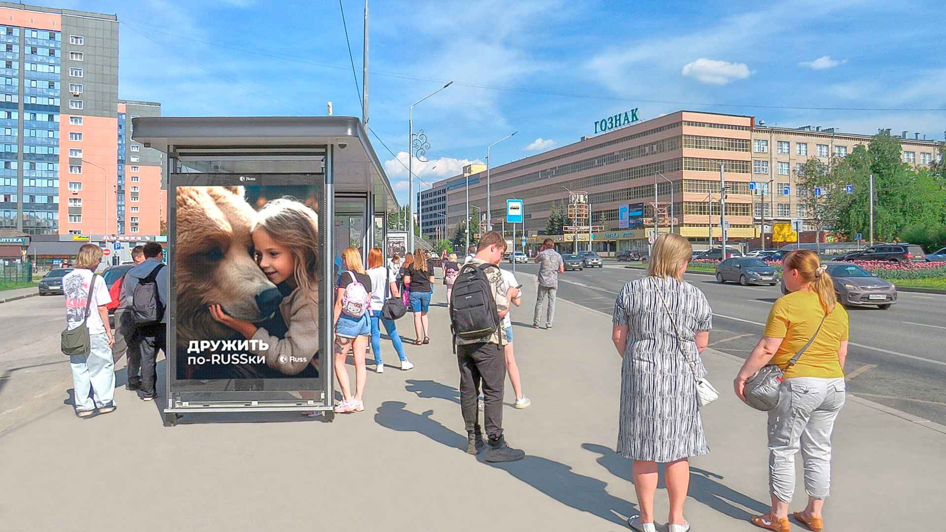 Pedestrians waiting at a bus stop on a sunny city street, with a large ad panel showing a girl hugging a dog. The ad includes Russian text at the bottom.