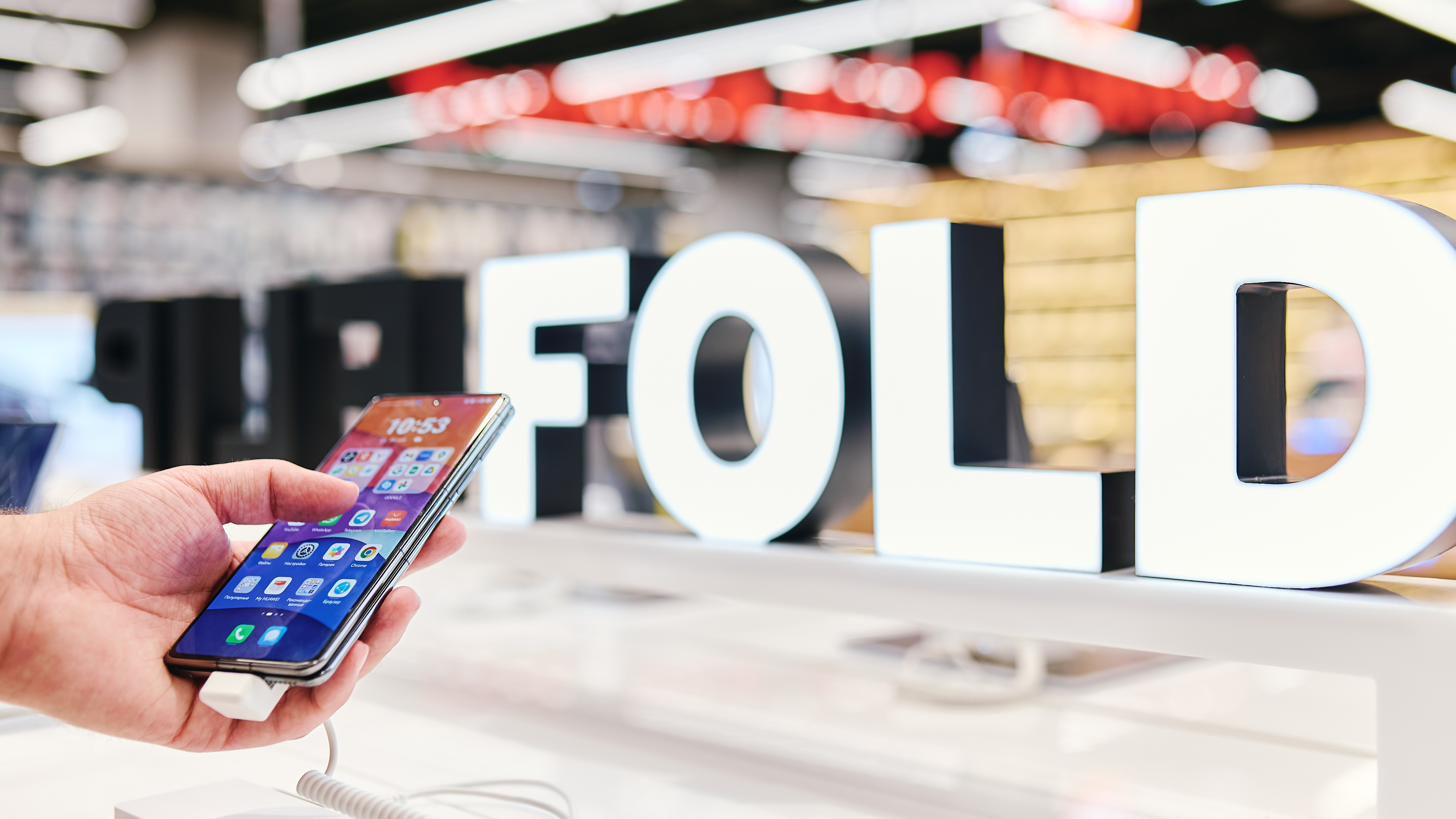 Close-up of a hand holding a smartphone on a store counter, screen showing app icons.