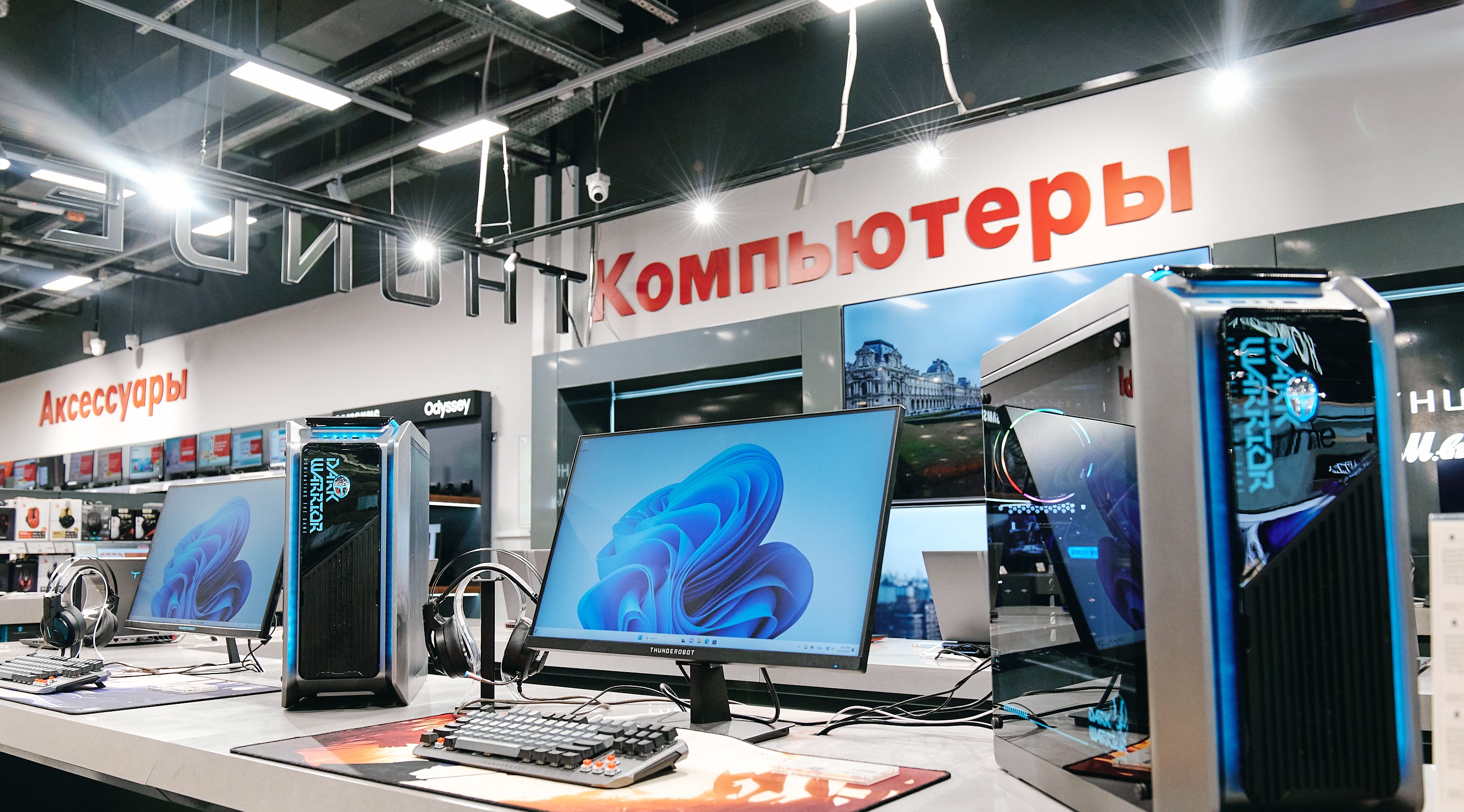 Row of desktop computers and monitors on a store counter, with red Russian signs reading 'Компьютеры' and 'Аксессуары' in the background