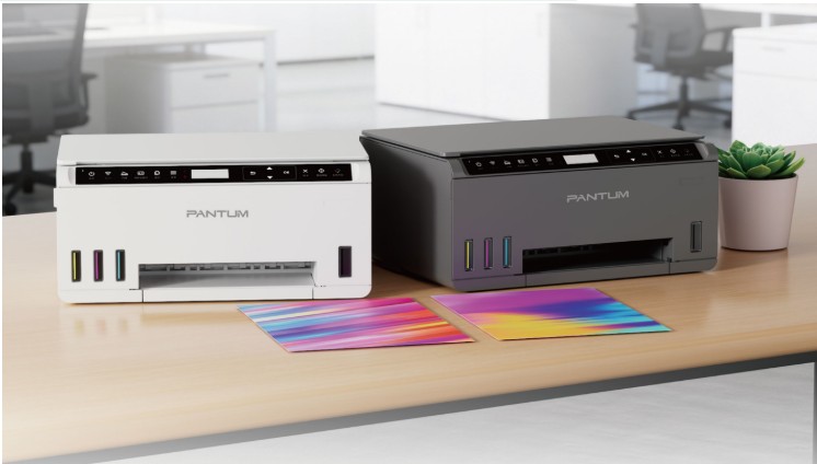 Two Pantum printers (white and dark gray) sit on a desk with colorful prints in front and a small plant in the background.