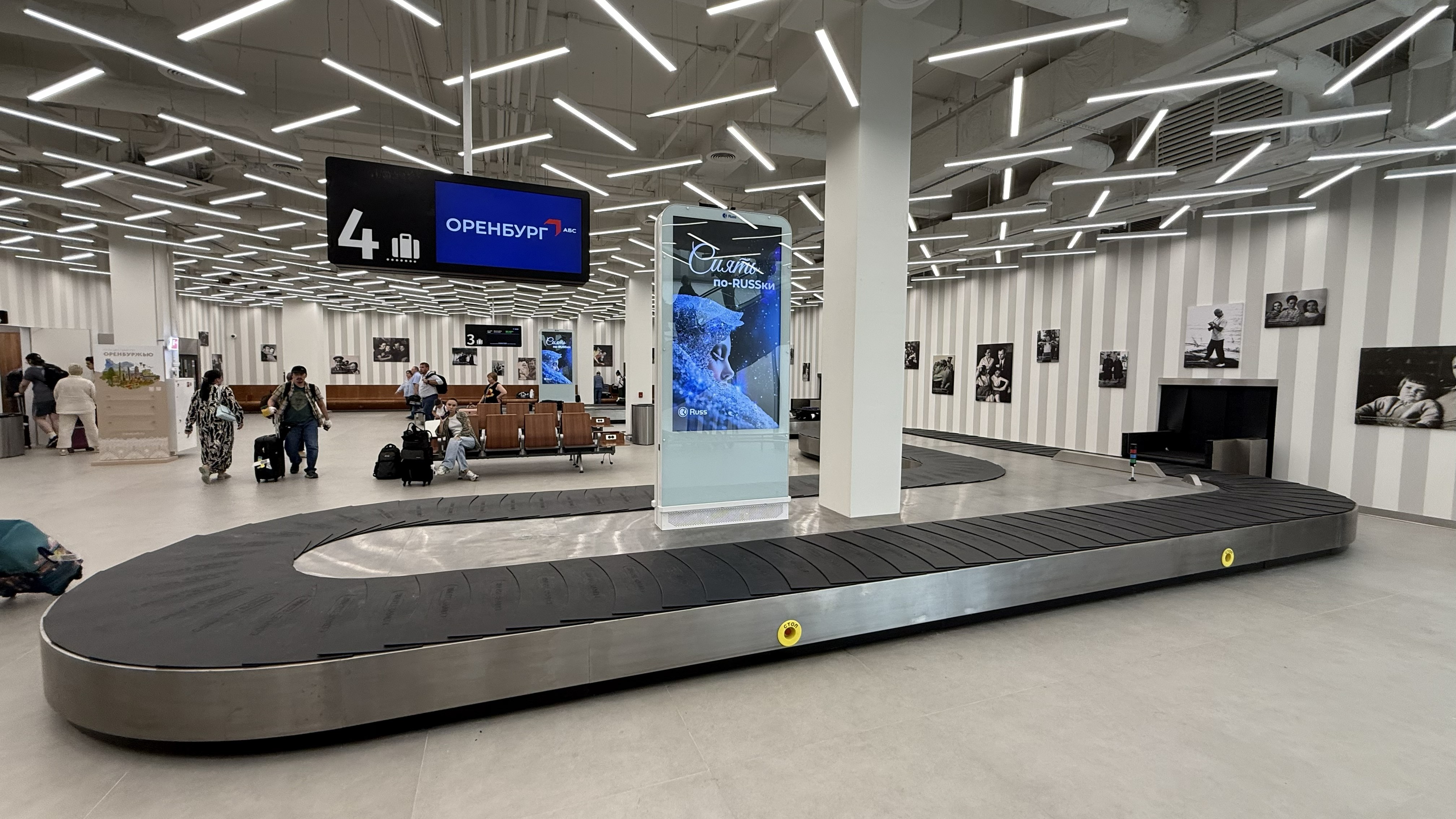 Airport baggage claim area with a large circular conveyor belt and travelers with suitcases waiting.