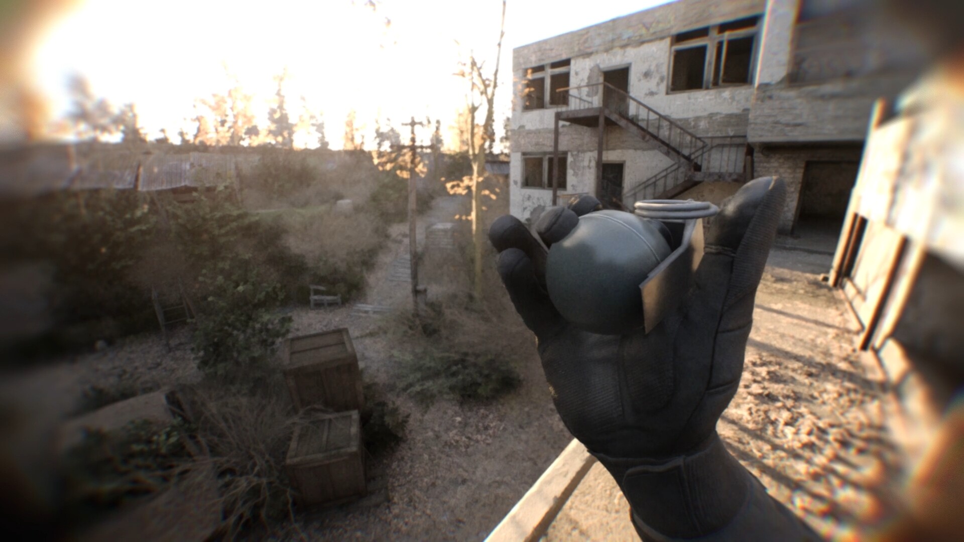 Gloved hand holds a gray hand grenade in a ruined outdoor setting with a two-story building in the background.